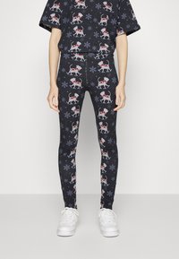 Leggings pretos com um padrão natalino apresentando cães brancos de cachecóis vermelhos e flocos de neve. Feitos de tecido elástico, com um design ajustado.