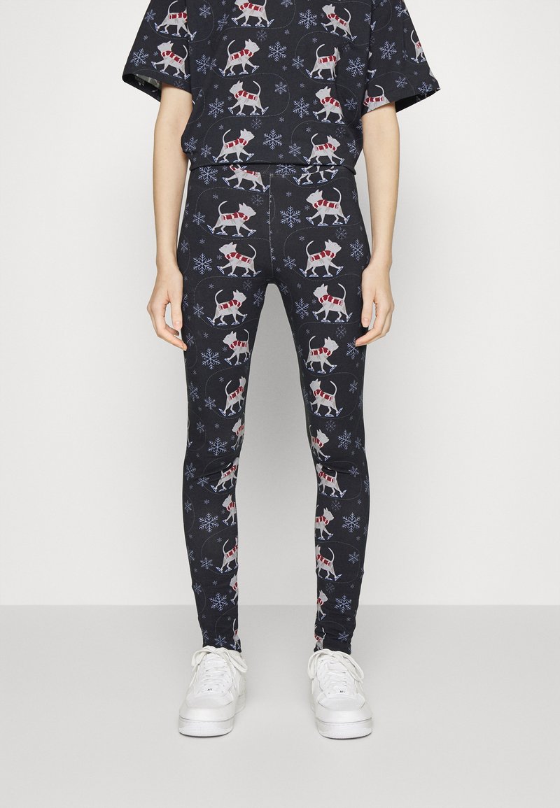 Leggings pretos com um padrão natalino apresentando cães brancos de cachecóis vermelhos e flocos de neve. Feitos de tecido elástico, com um design ajustado.