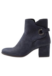 Botín de ante azul marino con un contorno curvado en la parte superior, un acento metálico redondo y un tacón grueso. Textura suave con un diseño elegante y moderno.