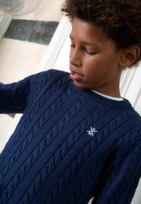 Sinine soonikudu kampsun tekstuuriga mustri ja soonikraega. Rinnal väike valge logo; valmistatud pehmest kudumismaterjalist.