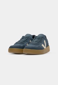 Sneaker in suede blu con accenti crema, punta rotonda, suola piatta in gomma e collo imbottito, caratterizzate da dettagli perforati e design con lacci.