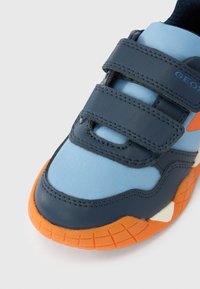 Μπλε και ναυ τικό αθλητικό παπούτσι με λουράκια βέλκρο και πορτοκαλί λεπτομέρειες. Υλικό με υφή, στρογγυλή μύτη και μοτίβο στη λαστιχένια σόλα.