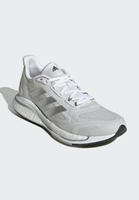 Weiße Sportschuhe mit Mesh-Obermaterial, strukturiertem Design, drei grauen Streifen und gepolsteter Sohle. Mit abgerundeter Zehenpartie und Schnürsystem.