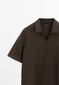 Korte mouw, donkerbruine overhemd met kraag, drie knopen en een omgeslagen mouwzoom, weergegeven tegen een witte achtergrond.