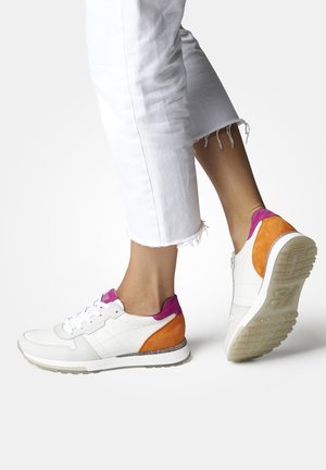 Sneaker bianco con accenti in suede rosa e arancione, tomaia in pelle bianca texturizzata, suola piatta e design con lacci. Jeans bianchi a cropped visibili.