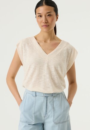 Top de color beige claro con escote en V, hombreras, tela texturizada y corte relajado. Combinado con pantalones de tiro alto en azul claro con bolsillos delanteros.