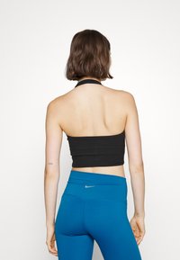 Top cropped preto com alças, feito de tecido elástico, combinado com leggings azuis de cintura alta que apresentam um pequeno logótipo da Nike na parte de trás.
