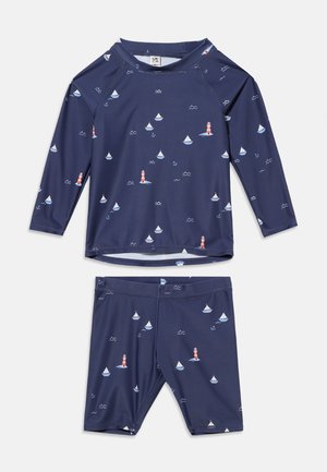 Marineblå langærmet badetrøje og shorts med sejlbåde, fyrtårne, ankre og bølgemønstre på stoffet.