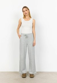 Pantaloni de trening gri deschis, cu picioare largi, talie elastică și șnur. Material moale; are buzunare laterale. Asortați cu un top alb fără mâneci.