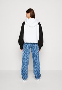 Hanorac supradimensionat alb și negru, cu glugă, asortat cu pantaloni lungi albaștri cu un model geometric. Tenisi albi vizibili.
