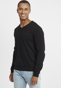 Black V-neck sweater in a soft knit fabric, featuring ribbed cuffs and hem, paired with light blue jeans. Simple, classic design.