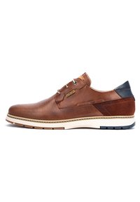 Zapato de cuero marrón con diseño perforado, tacón azul marino en contraste y suela de goma blanca. Presenta cierre con cordones y un sutil detalle de marca.