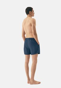 Granatowe kąpielówki z lekkiego materiału, o prostym designie, z elastycznym paskiem i bocznymi kieszeniami. Widok z tyłu.