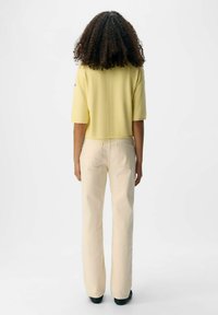 Geel cropped sweater met korte mouwen, gecombineerd met lichtbeige flare jeans. De stof lijkt zacht en het ontwerp is eenvoudig, wat zorgt voor comfort.
