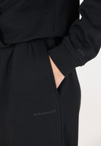 Zwarte hoodie met een geribbelde manchette en tailleband. Voorzien van een zijzak; het "ENDURANCE"-logo is subtiel in grijs gedrukt. Zacht, gestructureerd stof.