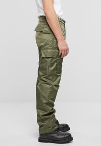 Pantalons cargo en vert olive, fabriqués dans un matériau lisse. Présentent plusieurs poches latérales, une coupe décontractée et sont associés à des bottes noires.