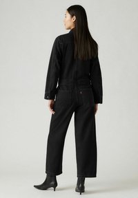 Czarny dżinsowy kombinezon z długimi rękawami, prostymi nogawkami, bocznymi i tylnymi kieszeniami, uzupełniony o botki za kostkę. Minimalistyczny design i szwy.