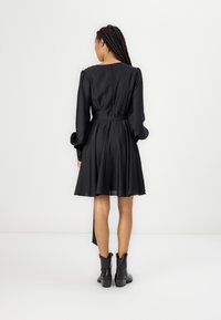 Robe en satin noir avec de longues manches bouffantes, corsage ajusté et jupe évasée. Comprend une ceinture à nouer à la taille et une fermeture en goutte d'eau dans le dos.