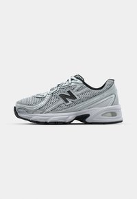 Stříbrná síťovaná sportovní bota s černými detaily, zaoblenou špičkou, polstrovanou podešví a šněrováním. Na boku má logo New Balance.