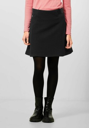 Jupe noire texturée avec un design évasé, dotée d'une large ceinture et de poches latérales, associée à des bottines noires et à des collants.