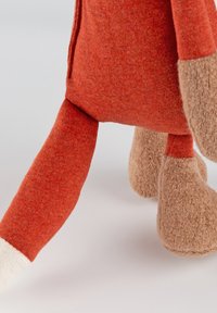 Un peluche con un corpo in tessuto arancione testurizzato, gambe in peluche marrone chiaro e un dettaglio a polsino bianco ai piedi.