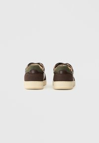 Sneaker in suede marrone con dettagli in pelle verde, suole in gomma crema e una silhouette slanciata caratterizzata da cuciture e design minimalista.