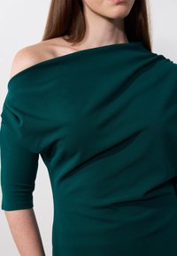 Teal off-shoulder topp i mjukt, fallande tyg; har en åtsittande passform med trekvartsärmar och slät yta.