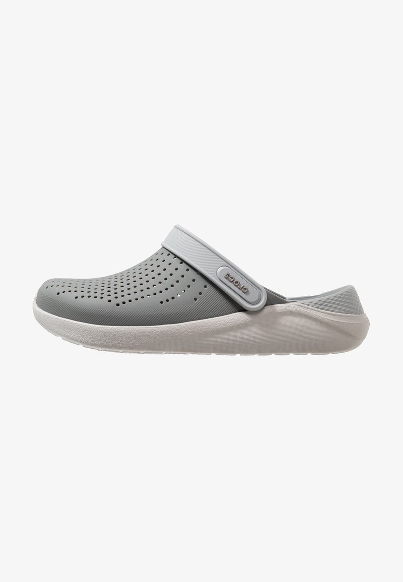 Sabot gris clair sans lacets avec trous de ventilation, bride de talon réglable et semelle blanche rembourrée pour un usage décontracté.