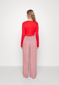 Red long-sleeve top paired with wide-leg, patterned pants featuring a floral design in red and white, with a relaxed fit and elastic waistband.