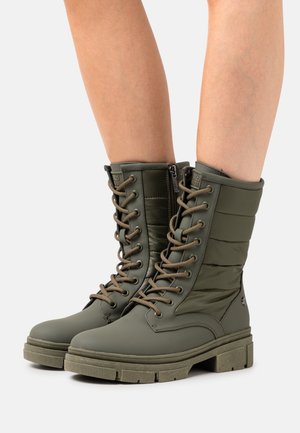 Botas impermeables verdes con parte superior de nailon acolchado, cierre frontal de cordones y suela de goma texturizada. Cuentan con cremallera lateral y tacón grueso.