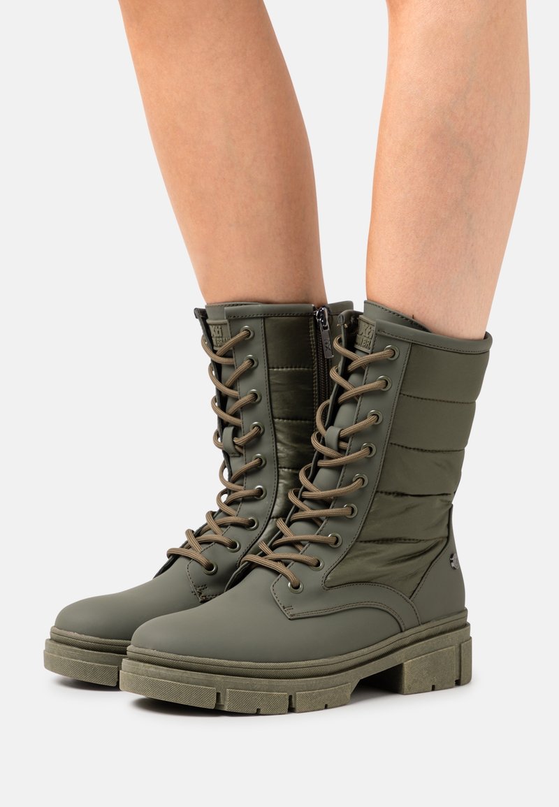 Bottes étanches vertes avec tige en nylon matelassé, laçage à l'avant et semelle en caoutchouc texturée. Dotées d'une fermeture éclair latérale et d'un talon épais.