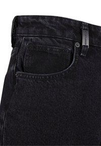Zwarte denim jeans met een textuurafwerking, zichtbare zakstiksels, metalen knoop en label bevestigd aan de tailleband.