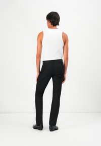 Black slim-fit jeans with back pockets, paired with a white tank top. Smooth fabric with minimal seams; worn with black shoes.