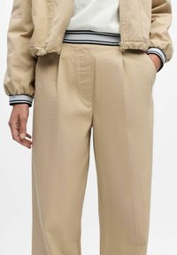 Beige broeken met een losse pasvorm, voorzien van een voorplooibaan, zijzakken en een elastische tailleband met zwart-witte strepen.