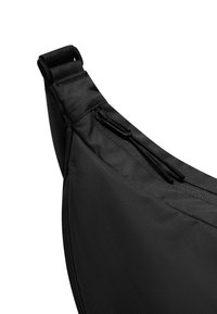 Czarna torba na ramię o smukłym, zaokrąglonym designie, wykonana z trwałego materiału, z kieszenią na zamek błyskawiczny i regulowanym paskiem dla wygody.