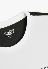 Camisa deportiva blanca con cuello negro, tejido texturizado y "Koton SPORT" impreso en la etiqueta interior. Talla pequeña.