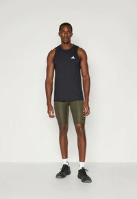 Czarny bezrękawnik z białym logo, zielone dopasowane szorty i czarne buty sportowe. Materiał wygląda na lekki i elastyczny.