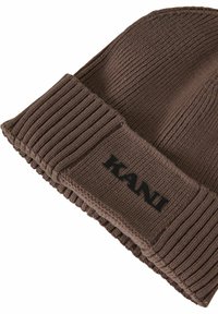 Beanie tricotat maro cu un manșon cu nervuri. Prezentând un material texturat și un logo negru "KANI" în față.