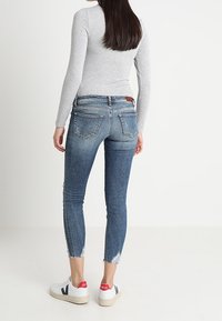 Jeans de mezclilla ajustados en un lavado intermedio, con un dobladillo descentrado y un desvanecimiento sutil. Combinados con zapatillas blancas con acentos rojos.