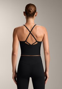Top sport negru, scurt, cu bretele încrucișate pe spate, realizat dintr-un material elastic. Textură netedă, design ajustat. Se potrivește cu colanți negri.