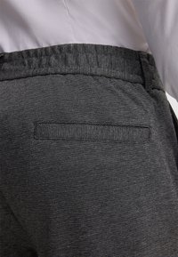 Pantalon gris foncé avec un tissage texturé, présentant une poche arrière et une taille élastique. Le matériau semble résistant et structuré.