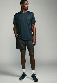 Mørkeblå, letvægts atletisk T-shirt med en subtil tekstur; parret med sorte shorts og marineblå sneakers, der har hvide sokker.