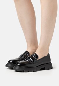 Zwarte gepatineerde leren loafers met een stevige rubberen zool en een ronde neus. Heeft twee banden over de wreef, wat textuur en detail toevoegt.