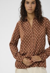 Braune Bluse mit Polka-Dots, Knopfleiste, langen Ärmeln und weichem Stoff. Mit Kragen und lockerem Schnitt.