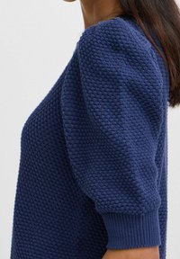 Náměsíčně modrý pletený svetr s texturovaným vzorem, balónovými rukávy a žebrovanými manžetami. Materiál vypadá měkký a teplý.