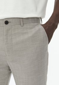 Hellgraue Leinenhose mit subtiler Textur, ausgestattet mit einem Knopfverschluss an der Taille und seitlichen Taschen.