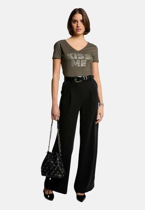 T-shirt ajusté vert olive avec le texte "KISS ME" en strass, associé à un pantalon large taille haute noir et un sac à main noir.