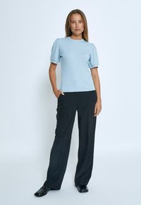 Gaiši zils ribots T-krekls ar īsām pūkainām piedurknēm, kopā ar melniem platām kājām biksēm un melniem apaviem, attēlots uz neitrāla fona.