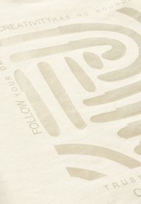 Bavlněná látka ve světle krémové barvě, s texturovaným grafickým designem v béžové barvě, včetně vlnitých linií a motivačního textu.
