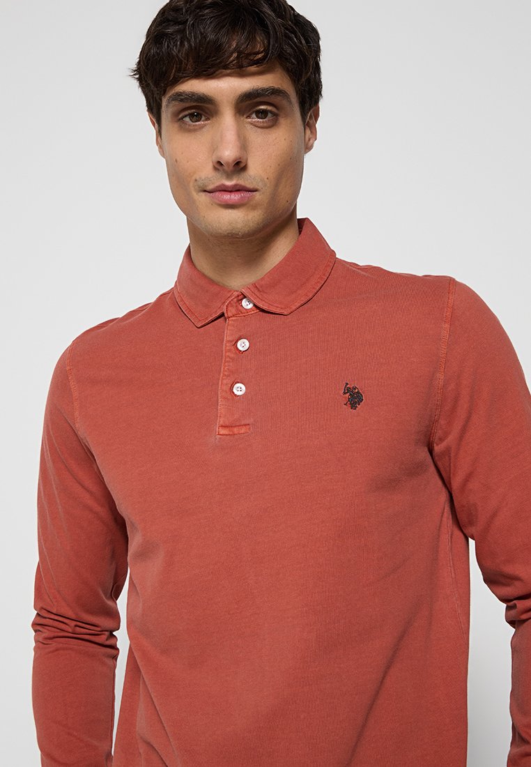 Langärmliges, rostfarbenes Poloshirt aus Baumwolle, mit einem Knopfkraagen und einem kleinen gestickten Logo auf der linken Brust.